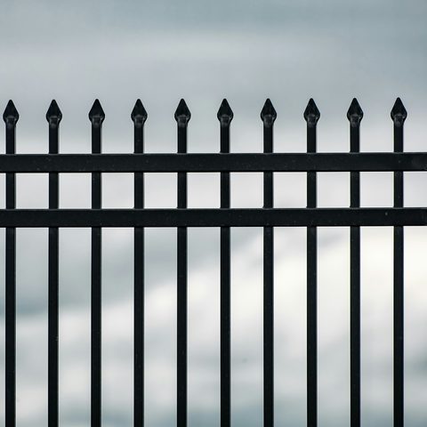 Black metal fence pickets with pointed finials against a gray sky