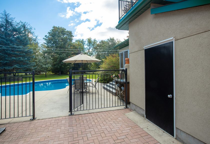 Black metal pool fence and gate between a brick patio and a pool deck