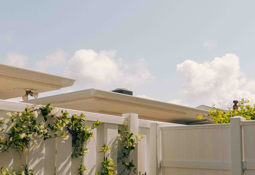 Cream-colored vinyl privacy fence with a flowering vine climbing it below a roofline